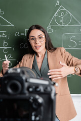 Teacher talking near math formulas on chalkboard and blurred digital camera in classroom