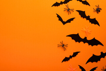 Orange Halloween background. Flock of black bats, spider, pumpkin, skeleton and leaves for Halloween. Black paper bat silhouettes on orange background. Autumn decoration. Halloween concept. Top view.