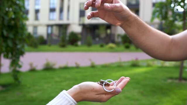 Close up of man hand passing key to woman on the street near the house - selling home. Buying dwelling - male realtor handing keys of new apartment to female customer. Real-estate agent job. Slow mo