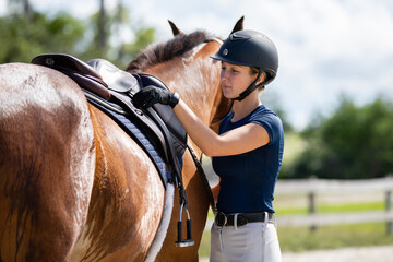 Equestrian adjusting her saddle and tack