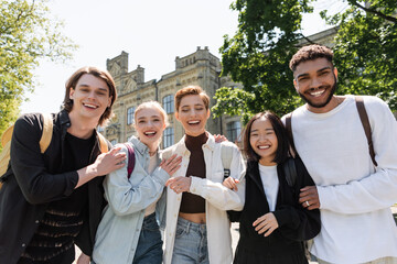 Obraz premium Positive multiethnic students hugging and looking at camera outdoors.