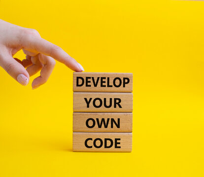 Develop your own code symbol. Concept words Develop your own code on wooden blocks. Beautiful yellow background. Businessman hand. Business and Develop your own code concept. Copy space.