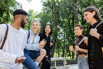Positive african american student using smartphone near interracial friends with coffee in park.