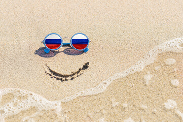 Fototapeta na wymiar A painted smile on the beach and sunglasses with the flag of the Russia. The concept of a positive holiday in the resort of the Russia.