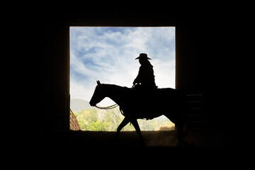 A cowgirl riders her horse by an open barn door. 