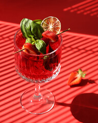 Drinks and beverages. Strawberry red cocktail with ice, lime, basil on a bright red background on a sunny day. Kitchen window sill. Background image, copy space