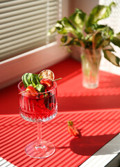 Drinks and beverages. Strawberry red cocktail with ice, lime, basil on a bright red background on a sunny day. Kitchen window sill. Background image, copy space