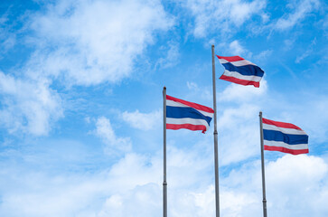 The flag of Thailand on a high pole with a bright sky and white clouds background.