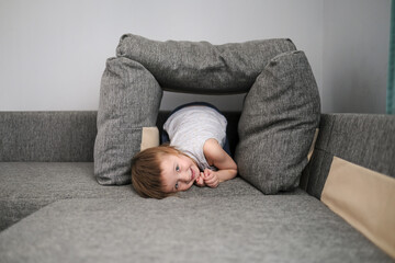 funny European child playing with pillows on couch