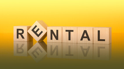 Obraz premium word Rental made with wood blocks. text is written in black letters and is reflected in the mirror surface of the table, yellow background