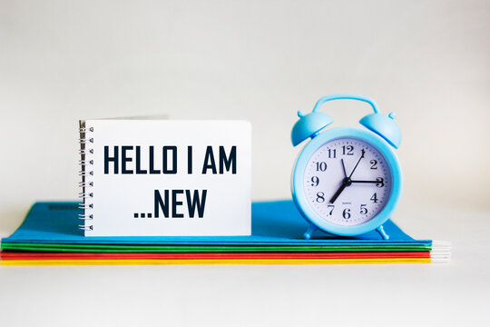 HELLO I AM NEW text on notepad with assorted folders and clock on white background