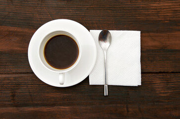Cap of a coffee, white serviette and tea spoon on a wooden desk