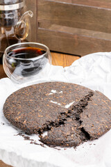Glass cup and teapot with chinese black pu-erh tea. Chinese tea ripe Puer in the form of a round pancake on the table