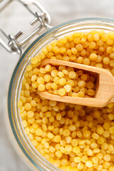 Ptitim. Dry uncooked ptitim pasta close-up in a glass jar with spoon. Israeli couscous