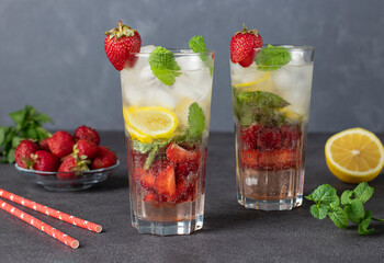 Cold bright strawberry Mojito cocktail with mint, lemon slices and ice cubes on gray background