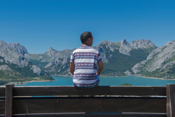 Fototapeta premium Chico joven observando las montañas de Riaño en desde un banco