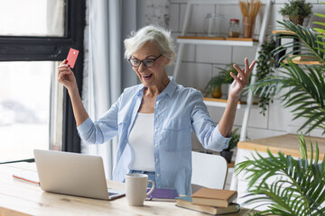 Beautiful senior woman with short grey hair and lovely smile shopping in the internet at home with a credit card. Concept of mature woman using technology