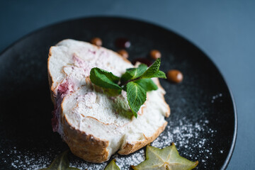 meringue roll cake with mascarpone cream, mint and carambola on black background