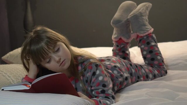 Little girl reading book and watching pictures in bed before going to sleep. 