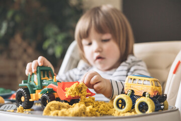 Cute little boy playing with kinetic sand, toy car and tractor. Development of fine motor skills....