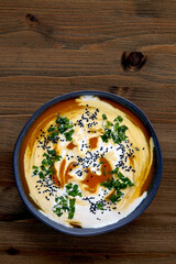 Bowl of creamy pumpkin soup with cream, black cumin seeds, herbs and cranberries on a wooden table