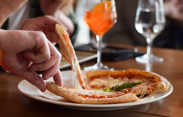 Persons hands separating pizza slices on plate in restaurant