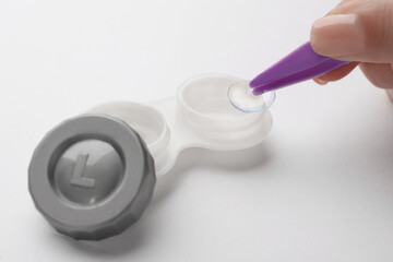 Woman taking contact lens from case with tweezers on white background, closeup