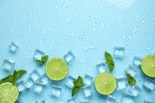 Ice cubes, mint and cut limes on turquoise background, flat lay with space for text. Refreshing drink ingredients