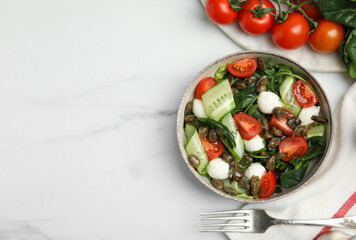 Salad with vegetables, capers and mozzarella in bowl on white marble table, flat lay. Space for text