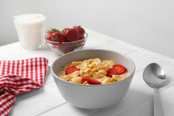 Corn flakes with strawberries in bowl served on white wooden table