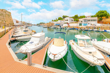 Fototapeta na wymiar Boats line the picturesque marina port harbor at Ciutadella de Menorca, Spain, a small Balearic island in the Mediterranean Sea, with the colorful village in view.