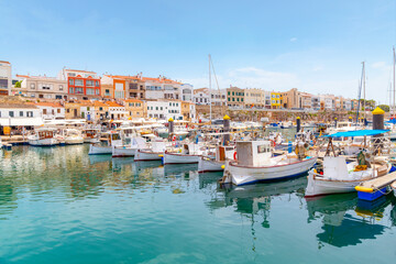 Fototapeta na wymiar Boats line the picturesque marina port harbor at Ciutadella de Menorca, Spain, a small Balearic island in the Mediterranean Sea, with the colorful village in view.