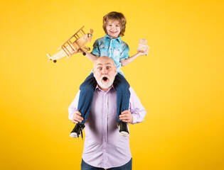 Grandson child and grandfather piggyback ride with plane and wooden toy truck. Men generation granddad and grandchild.