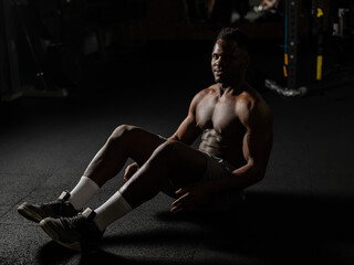Fototapeta na wymiar Afro american man doing abdominal exercises in a dark studio. 