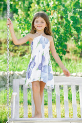 Fashion kids dress. Happy little child girl on a swing in the summer park. Happy kid having fun outdoors.