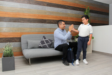 Obraz premium Latin dad with his overweight son prepare for back to school with uniform, and backpack show their love in the living room 