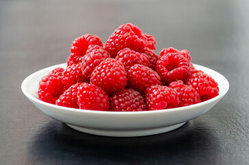Raspberries on a white plate. Dark background. Close up
