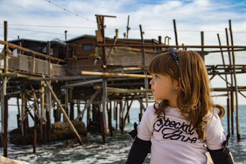 Image of an adorable little girl sitting on a cliff by the sea with overflowing background....