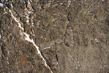 Rock texture. Snow and cracks on the surface of the cliff. Natural stone background.