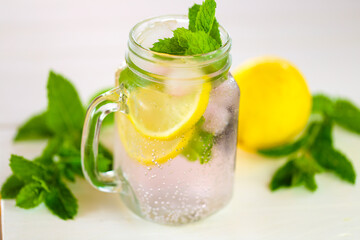 Lemon mint water with ice in a transparent misted mug.Citrus cocktail with mint leaves. Sassy lemon water.Lemon summer drink.Dietary lemon drink. ice falls into a glass with a cocktail.Sprig of mint