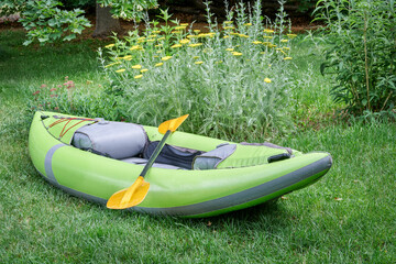 green inflatable whitewater one person kayak with a paddle in a backyard ready for a paddling...