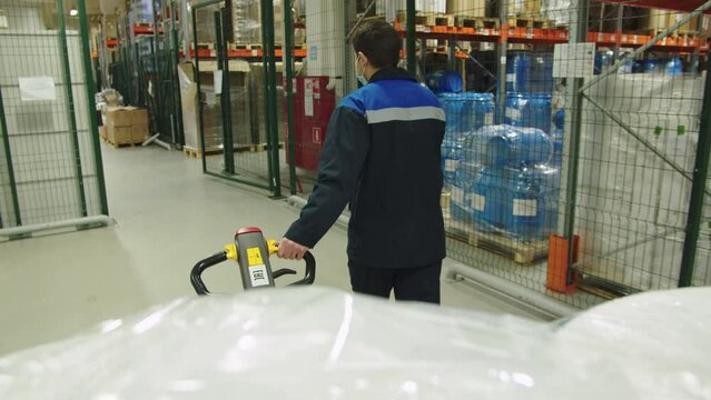 Back view of forklift operator in special uniform pulling the batch of packaged containers of medicine. loader transports cargo trolley at the producing warehouse.