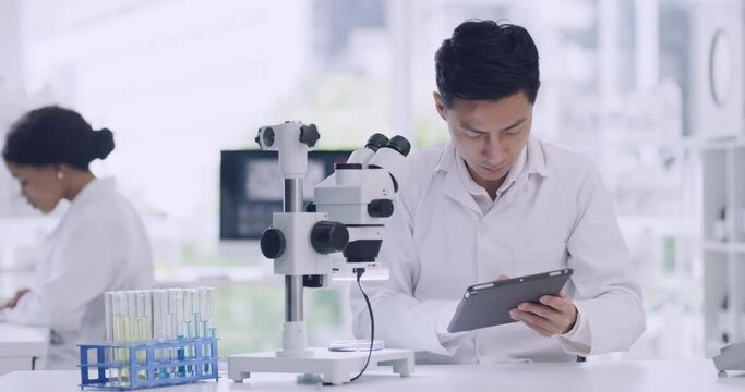 Leading scientist using a microscope and digital tablet in a lab. Focused man looking at medical samples, keeping record or test results on a device. Handsome chemist discovering a cure or treatment