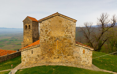Obraz premium Spring landscape with view of ancient structures built of rubble with tiled roofs on territory of Nekresi monastery on top of wooded hillock of Nazvrevi Gora, Qvareli Municipality, Georgia