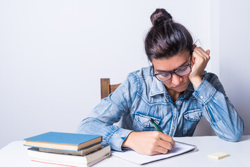 latina woman, studying at home, seated, with glasses, bored looking at her book, college concept
