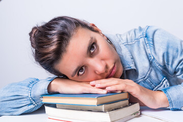 latina woman, studying at home, seated, close up, lying on top of her books, looking straight ahead, college concept