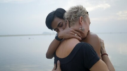 Bust shot of Thai young man and mature caucasian woman kissing at seaside sunset beach - slow motion
