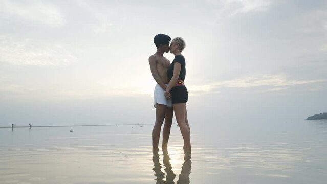 Silhouetted Couple kissing at sunset standing in shallow calm sea water with sunlight reflection on water surface