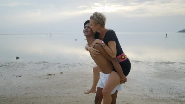 Lovely Interracial couple piggyback ride and kissing at the beach at sunset