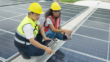 A senior Asian engineer and a young woman are using a laptop to check the solar panels.